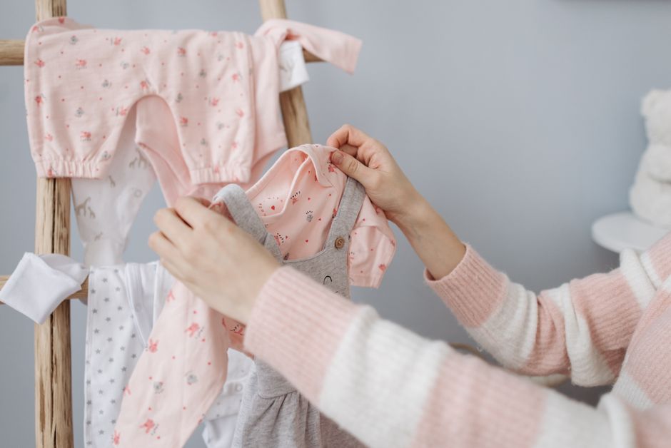 A mother organizes adorable baby clothes on a wooden rack indoors.