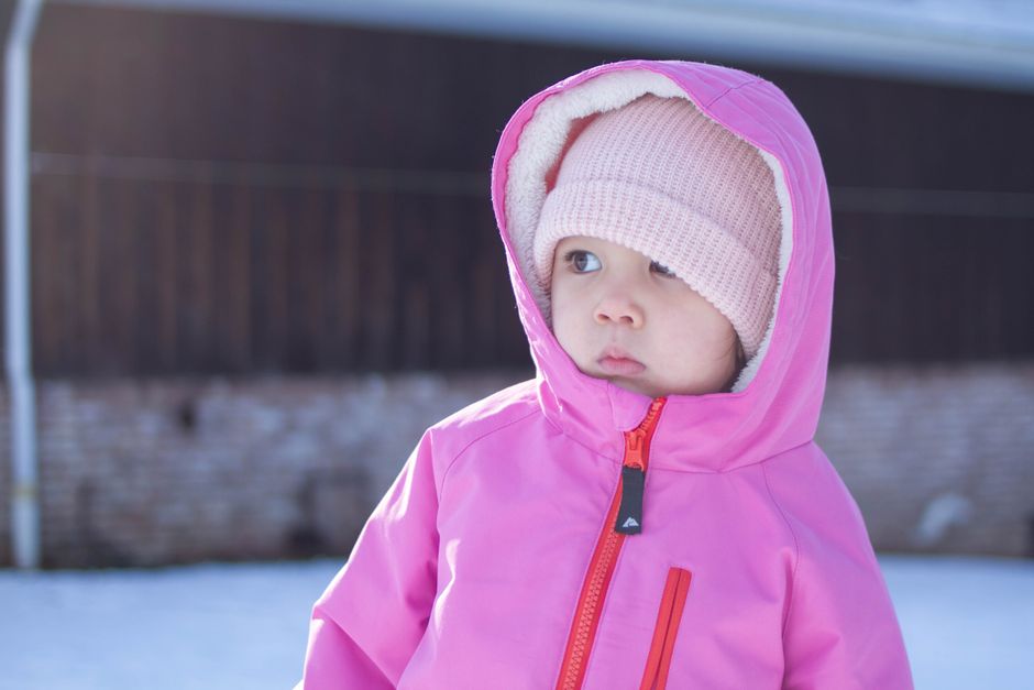 Adorable toddler enjoying a snowy day in a pink winter coat and wool hat.